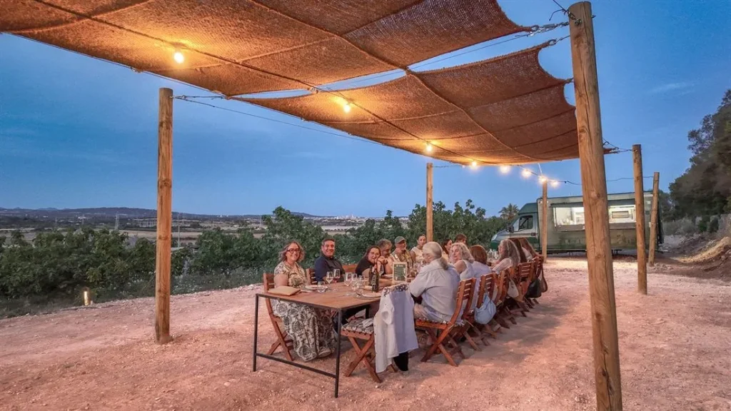 A group sharing a long table under a lighted awning in the Mallorcan countryside